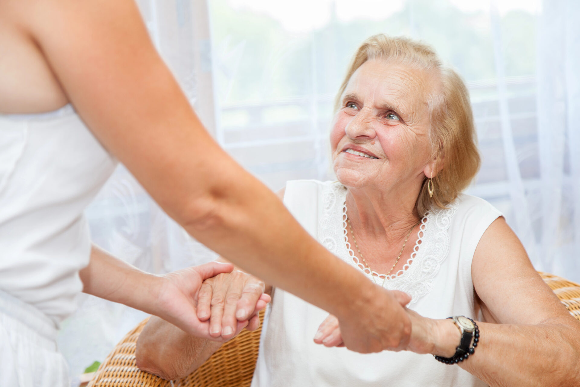 Cuidadora a segurar as mãos de uma senhora idosa sentada numa cadeira